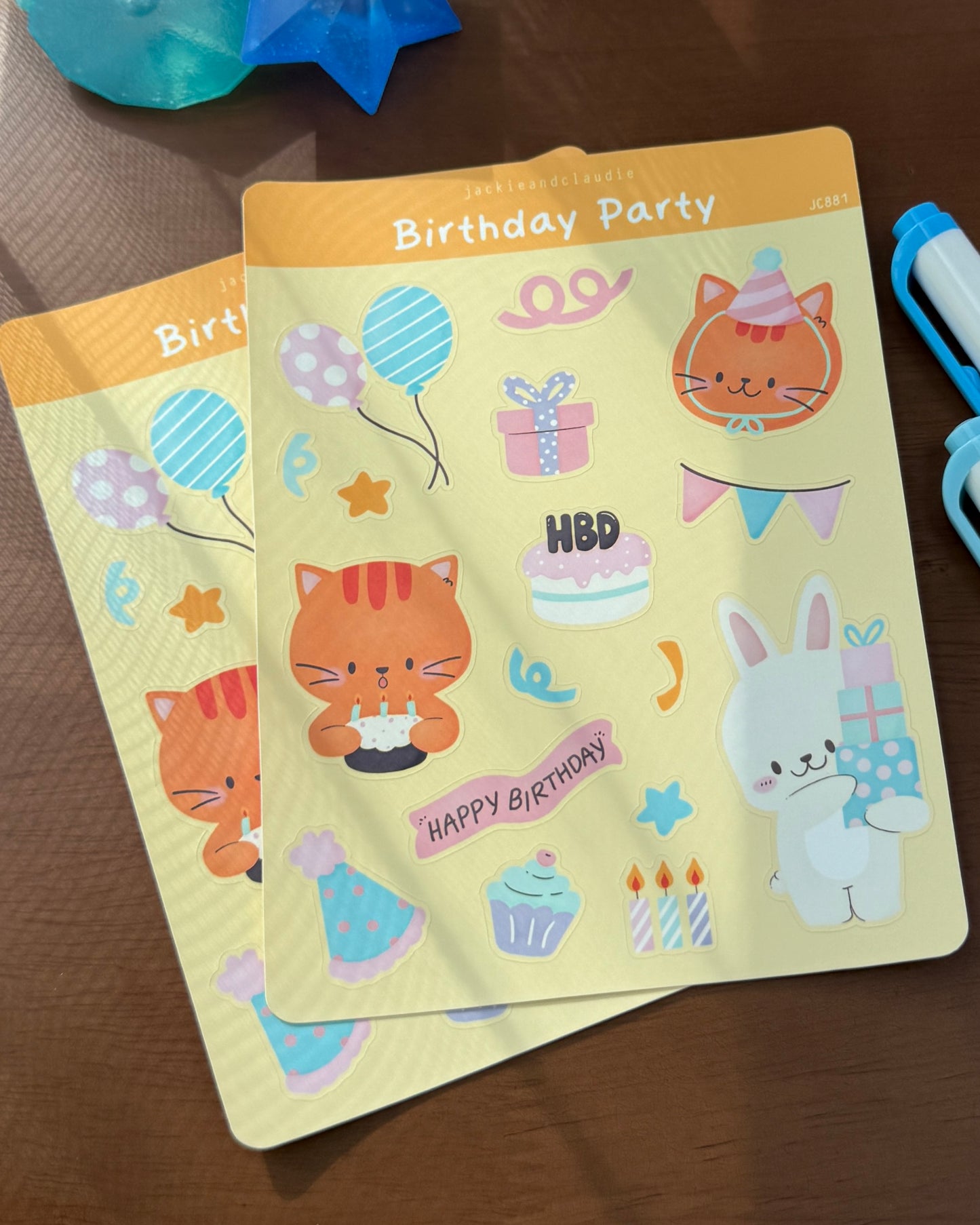 Two birthday-themed stickers with cartoon animals and text on a wooden surface.