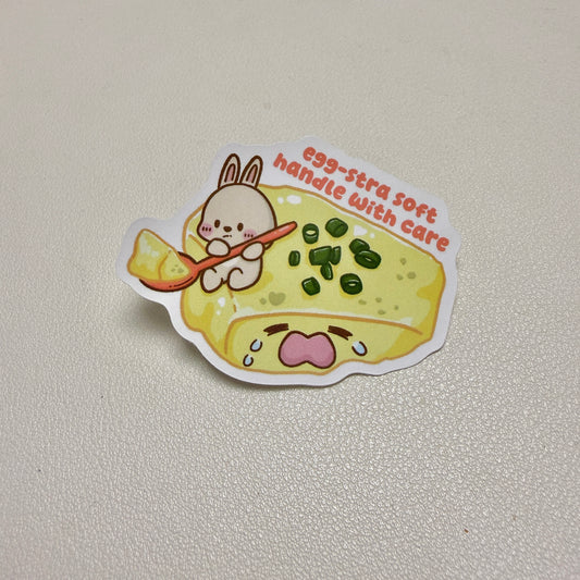 sticker of rabbit scooping a crying steamed egg with text 'egg-stra soft handle with care'