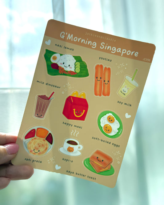 Card with cartoon illustrations of Singaporean breakfast items held against a light curtain background.