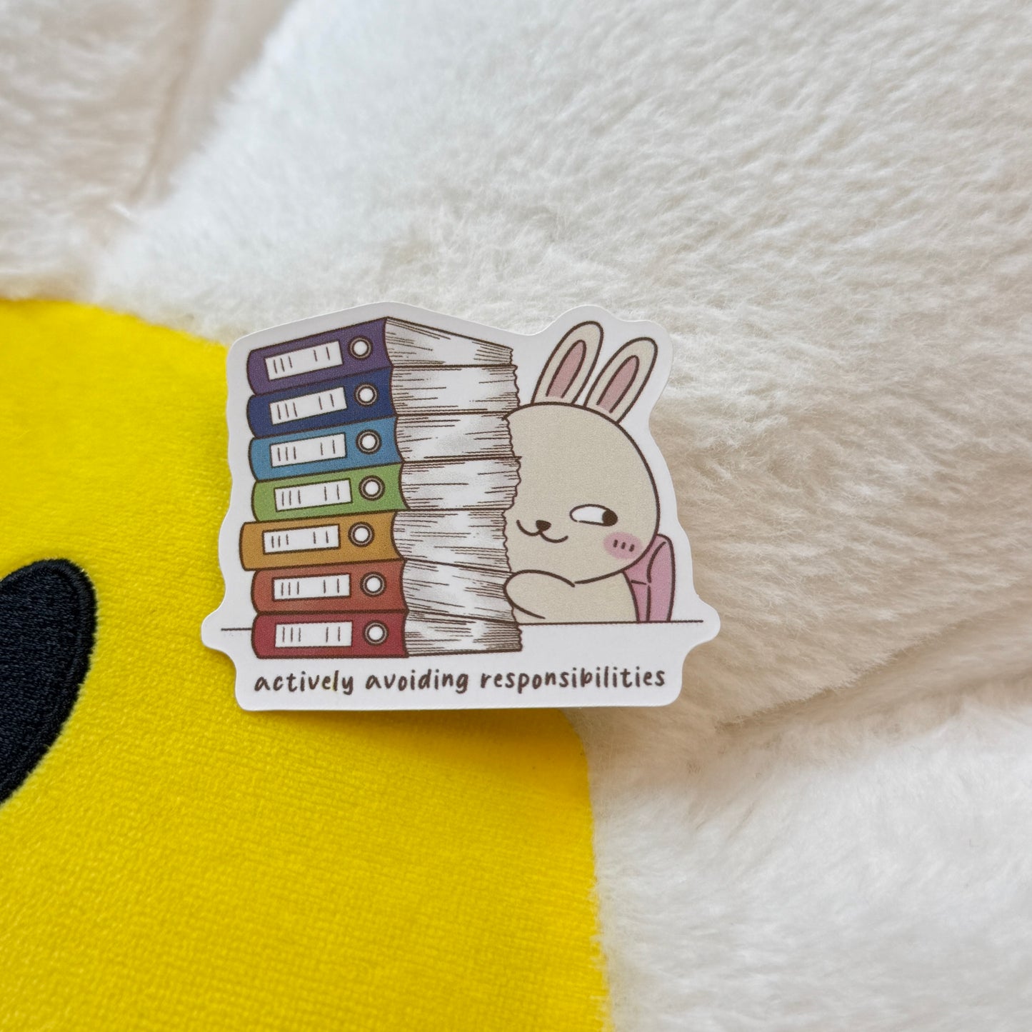 Sticker of a cartoon rabbit with books and text 'Actively avoiding responsibilities'