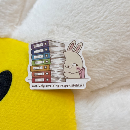 Sticker of a cartoon rabbit with books and text 'Actively avoiding responsibilities'