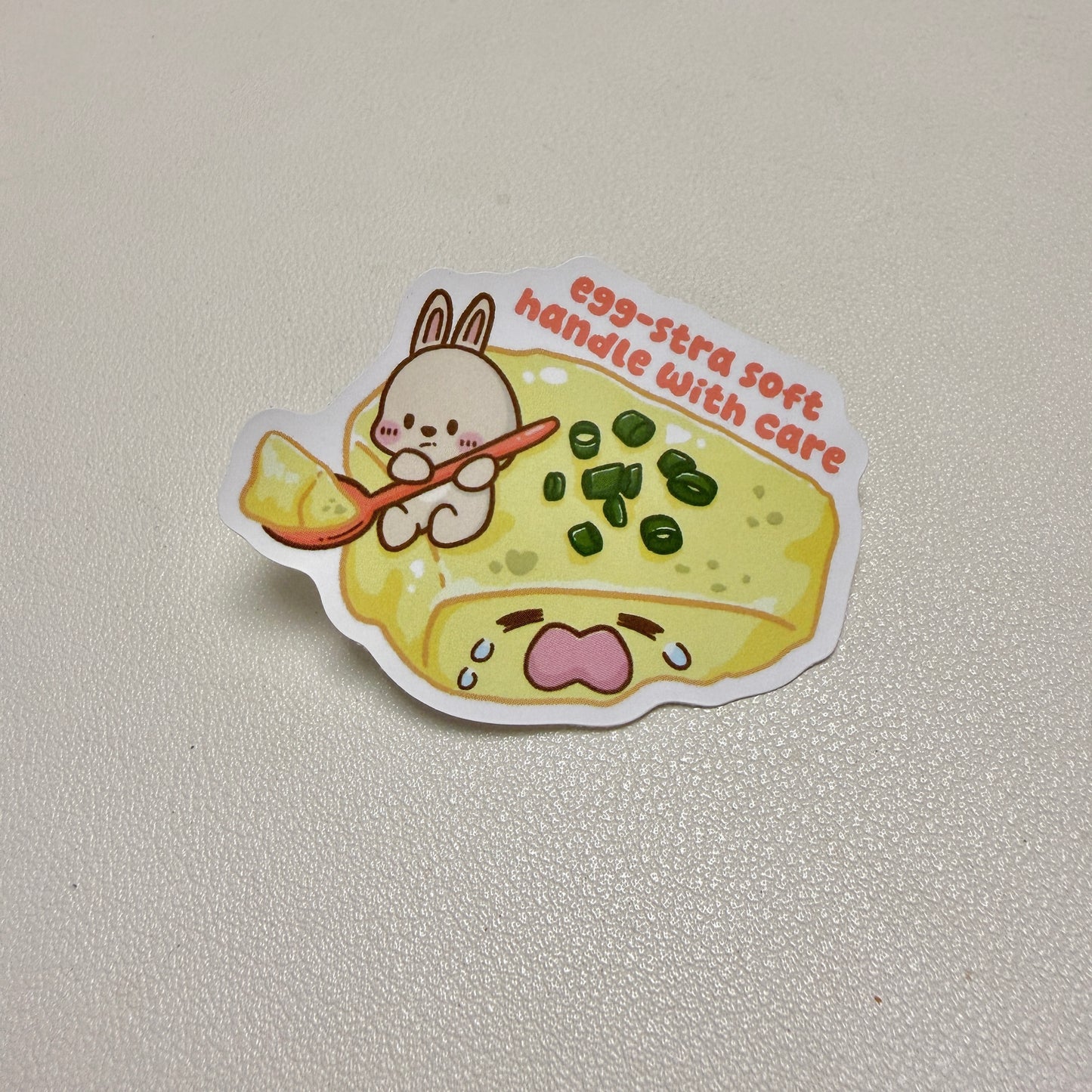 sticker of rabbit scooping a crying steamed egg with text 'egg-stra soft handle with care'