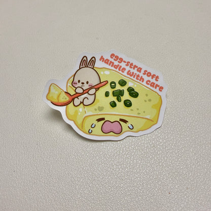sticker of rabbit scooping a crying steamed egg with text 'egg-stra soft handle with care'